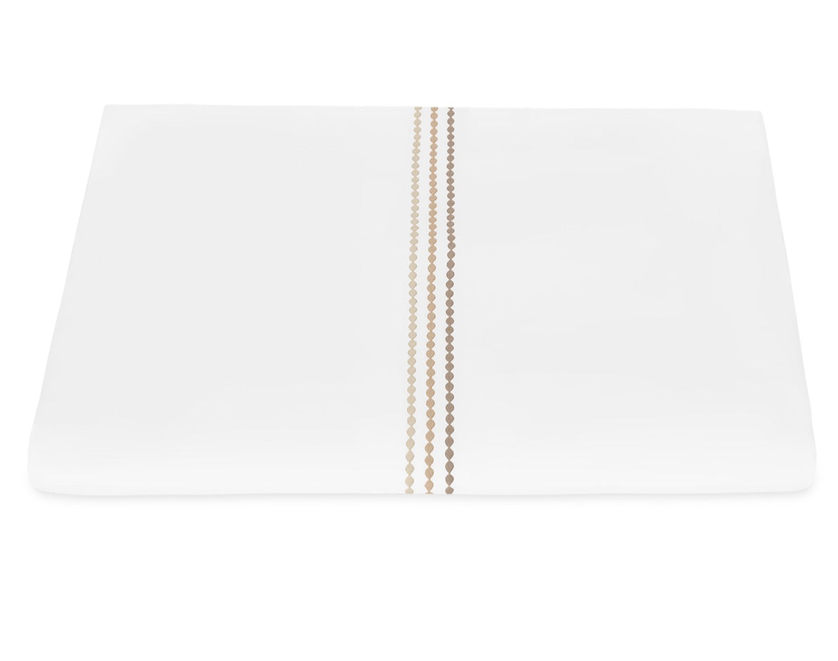 The Amara Triple Pearl Bedding Collection by Matouk features luxurious Amara sateen in crisp white, adorned with two vertical rows of tan circular embroidery near the center, evoking a triple pearl motif against a pristine background.