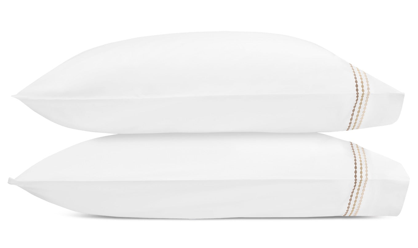 Two white pillows from the Matouk Amara Triple Pearl Bedding Collection are stacked horizontally, each showcasing a triple pearl embroidered motif with three parallel tan stitched lines near one end, set against a plain white background.