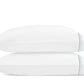 Two white pillows from the Matouk Amara Triple Pearl Bedding Collection, featuring elegant blue stitched stripes near the edge and a refined triple pearl embroidered design, are stacked on top of each other against a plain white background.