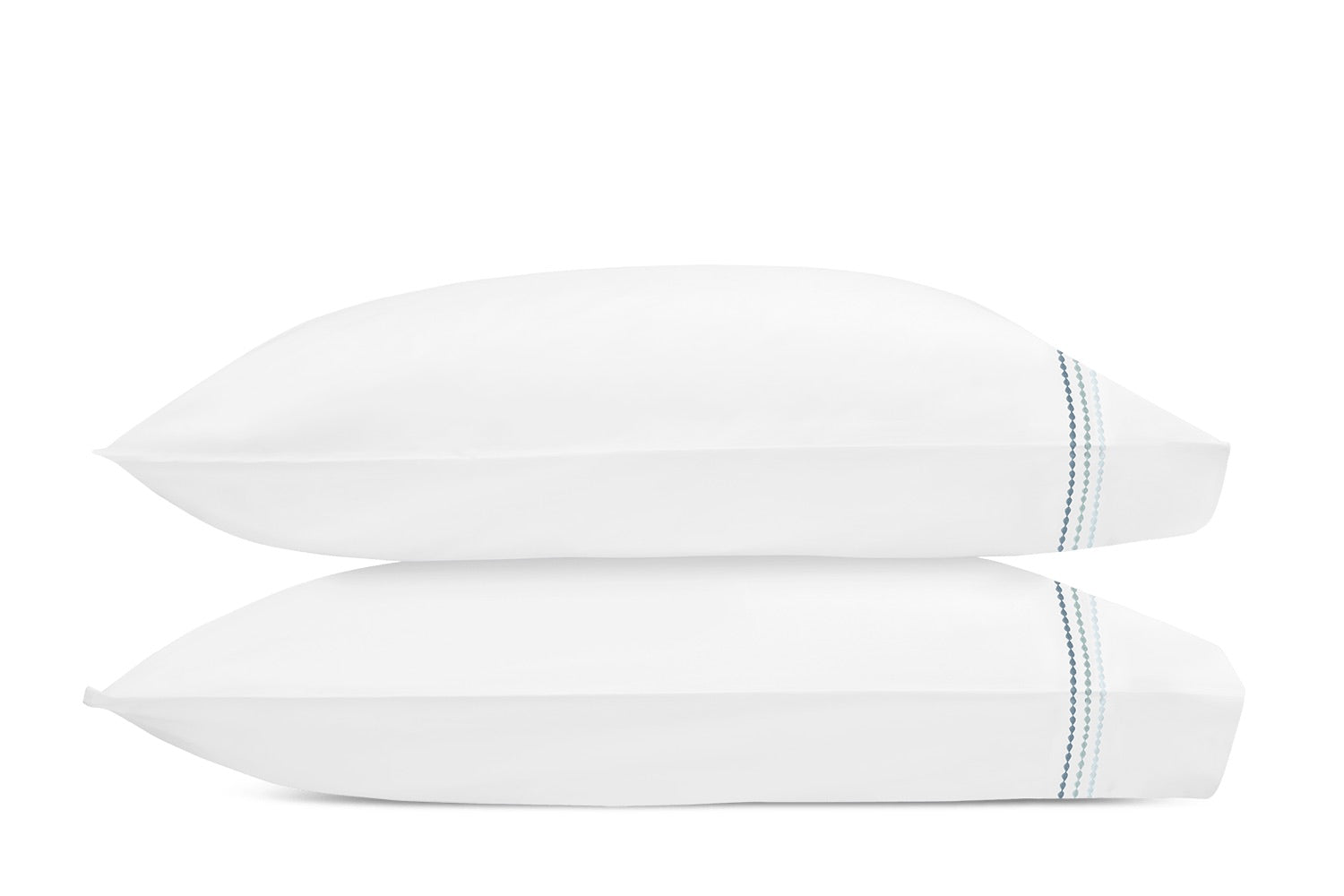 Two white pillows from the Matouk Amara Triple Pearl Bedding Collection, featuring elegant blue stitched stripes near the edge and a refined triple pearl embroidered design, are stacked on top of each other against a plain white background.