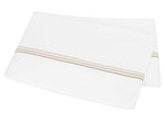 A folded white bedsheet from the Amara Triple Pearl Bedding Collection by Matouk, crafted from luxurious sateen and adorned with an elegant embroidered horizontal stripe of small beige and brown dots near one edge, displayed on a plain background.
