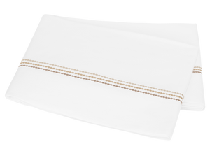 A folded white sheet from the Amara Pearl Bedding Collection, Beach by Matouk, featuring an elegant sateen finish and two tan embroidered lines, placed on a white background.