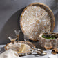 The Mya Inlay Serving and Decor Collection by Be Home features a round acacia wood and mother of pearl tray with a gold and white leaf pattern, holding cheese, napkin, and glassware; matching salad bowl and tray sit nearby against a gray background.