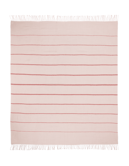 A square, light pink Matouk Amelia Stripe Throw with evenly spaced horizontal red stripes and white fringe on two edges is laid flat on a green background.