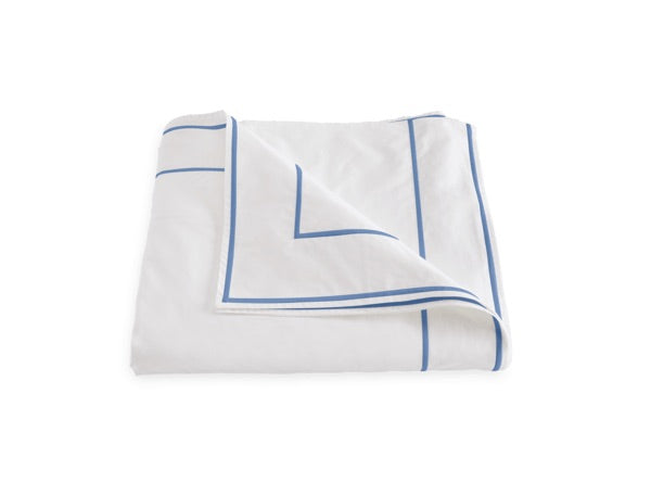 The Ansonia Bedding Collection by Matouk features luxury bedding crafted from premium cotton percale, showcasing a crisp white sheet or blanket adorned with refined blue line borders and delicate satin stitching—an elegant choice for those seeking sophisticated style.