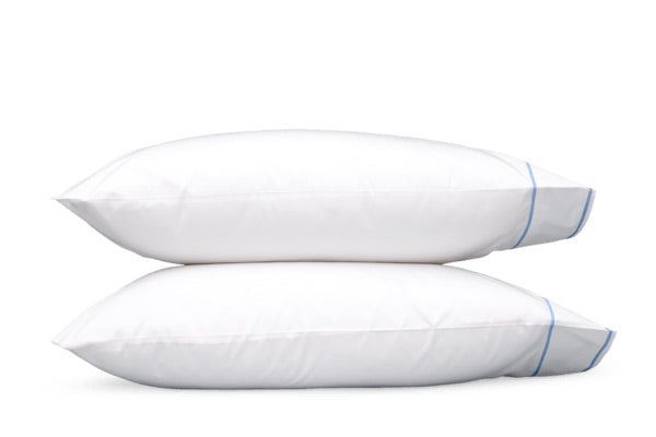 Two white Ansonia Bedding Collection pillows by Matouk, featuring blue piping and crafted from crisp cotton percale, are stacked horizontally on a white background.