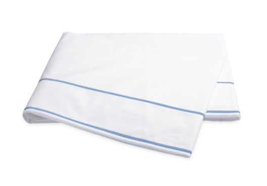 The Matouk Ansonia Bedding Collection features a folded white bed sheet crafted from soft cotton percale, accented by two parallel light blue lines near the edge finished in elegant satin stitching, displayed on a plain background—a perfect touch of luxury bedding for any refined space.