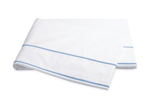 The Matouk Ansonia Bedding Collection features a folded white bed sheet crafted from soft cotton percale, accented by two parallel light blue lines near the edge finished in elegant satin stitching, displayed on a plain background—a perfect touch of luxury bedding for any refined space.