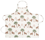 The Matouk Linen Apron Collection features a white linen apron with two front pockets, adjustable neck and waist straps, and an all-over pattern of tigers, palm trees, and red flowers inspired by Schumacher prints.