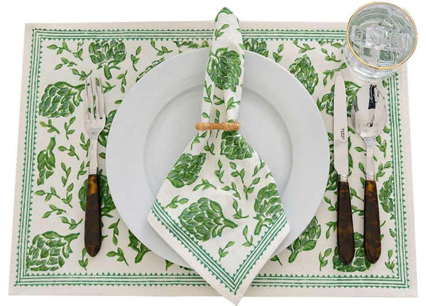 Elegant table setting with Pomegranate Inc.'s Dancing Artichokes Collection placemat and napkin, featuring hand-painted globe artichokes, white plates, and silverware, accompanied by a water glass.