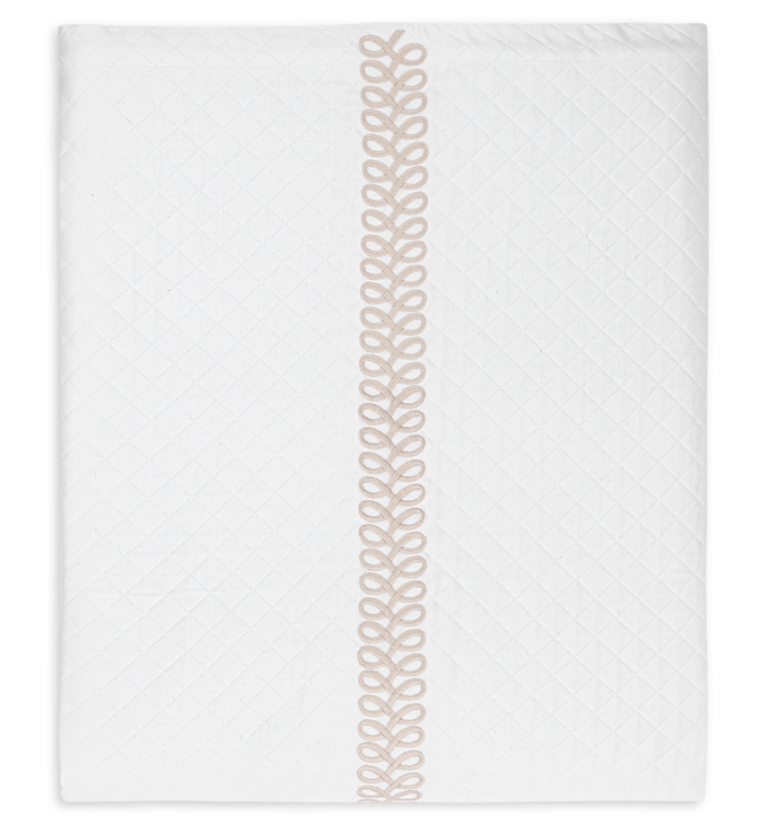 A folded white Matouk Astor Braid Matelassé quilt from the Dune collection, featuring a subtle diamond pattern and a vertical beige embroidery loop design in the center.