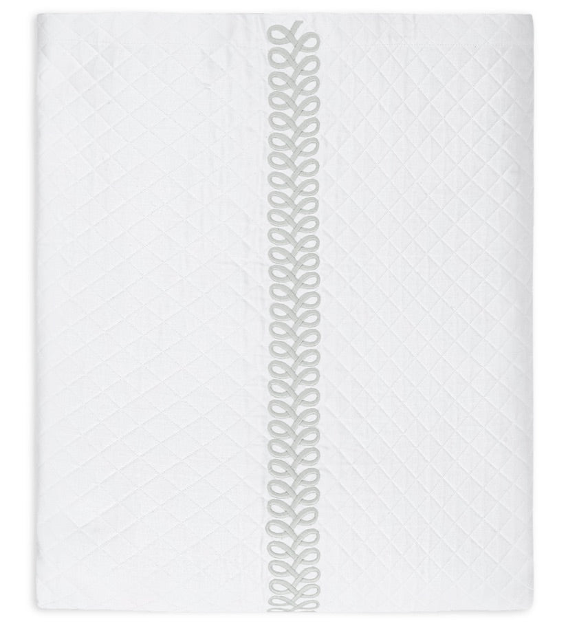 Introducing the Astor Braid Matelassé Bedding Collection by Matouk—a white quilted blanket adorned with a diamond pattern inspired by the Petra diamond matelassé. This refined piece features the signature Astor Braid embroidery as a vertical decorative looped trim down the center, exemplifying elegant craftsmanship from Matouk.