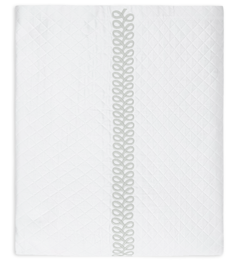 The Astor Braid Matelassé Bedding Collection in silver by Matouk features a diamond-patterned quilt with a single decorative stitched strip running vertically down the center.