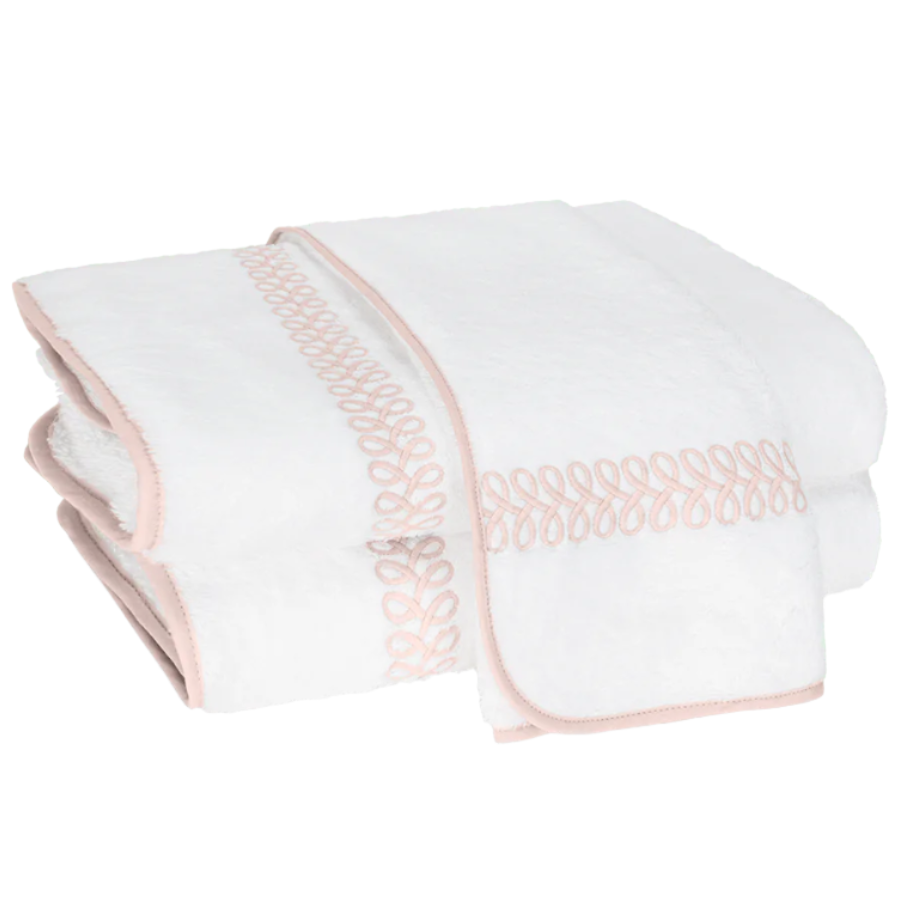 Two folded white towels from the Matouk Astor Braid Bath Collection, featuring pink embroidery and edging, crafted from luxurious long-staple cotton, are stacked neatly.