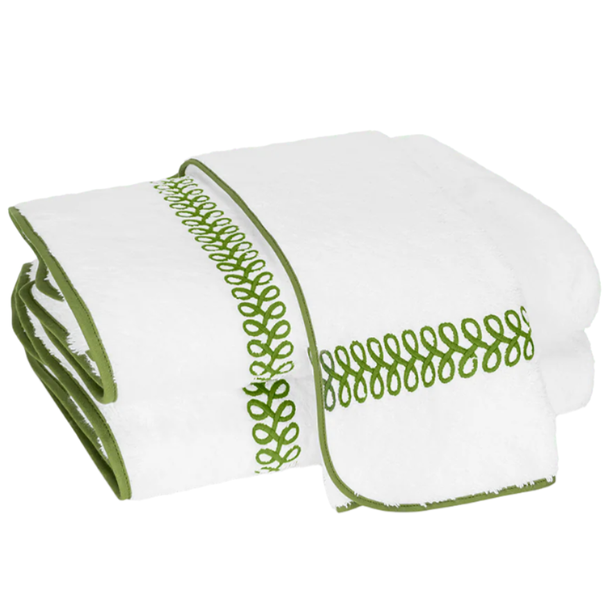 The Matouk Astor Braid Bath Collection features a folded white long-staple cotton towel with a green looped embroidery pattern and matching green Astor Braid trim along the edges.