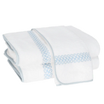 A folded towel from the Matouk Astor Braid Bath Collection, crafted of luxurious long-staple cotton with light blue embroidered Astor Braid loops and blue trim, is displayed on a white background.