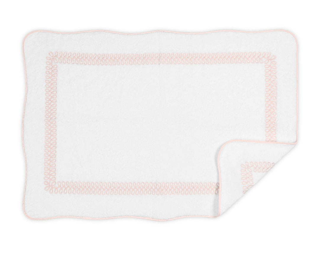 The Matouk Astor Braid Bath Collection features a white rectangular blanket crafted from long-staple cotton with a subtle pink embroidered border, scalloped edges, and one corner folded to show the reverse side.