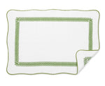 The Astor Braid Bath Collection by Matouk features a white rectangular bath mat with scalloped edges, made from long-staple cotton Cairo terry, detailed with a green looped border and a corner turned up to show the reverse pattern.