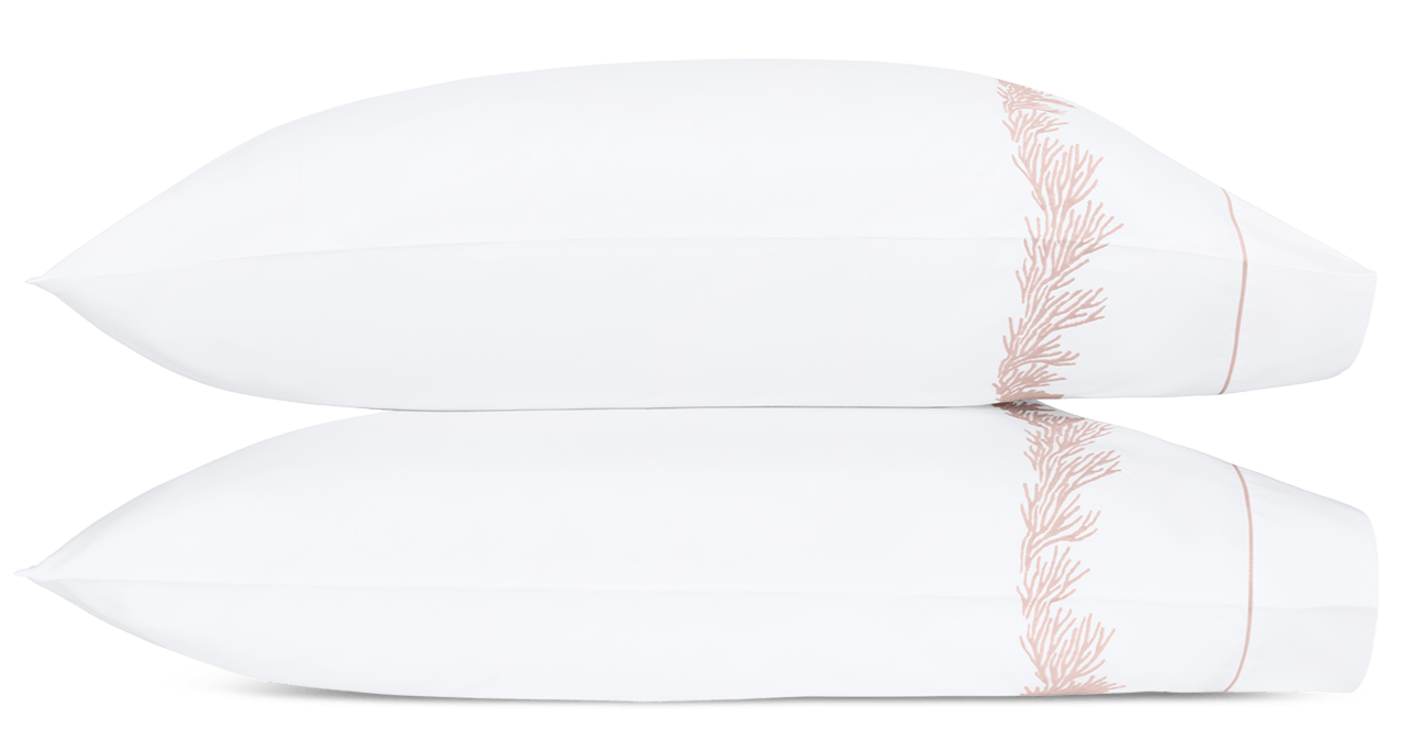 Two white pillows from the Atoll Bedding Collection, Blush by Matouk, made of Ceylon cotton percale with feathery coral embroidery on one end, are stacked against a white background.