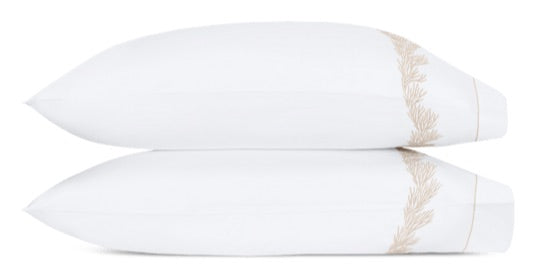 Two white pillows from the Atoll Bedding Collection by Matouk, featuring beige decorative trim and expertly crafted from luxurious 520 thread count CEYLON cotton percale, are stacked neatly on top of each other against a plain white background.