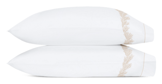 Two white pillows from the Atoll Bedding Collection, Dune by Matouk, featuring a beige embroidered pattern and crafted from luxurious Ceylon cotton percale, are stacked together.