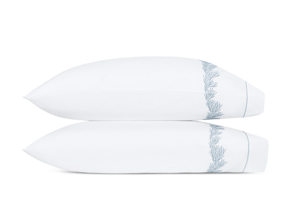Two white pillows from the Atoll Bedding Collection by Matouk for Wedgwood, stacked horizontally, each featuring a blue embroidered pattern and a satin stitch border for elegant detail.
