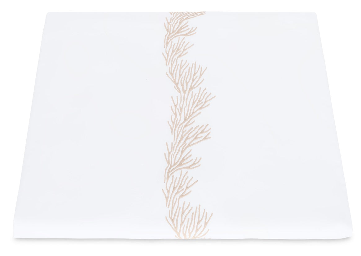 The Atoll Bedding Collection by Matouk features a white table runner adorned with a beige, coral-inspired embroidered motif down the center, meticulously crafted from luxurious CEYLON cotton percale with a 520 thread count for an elegant and refined finish.