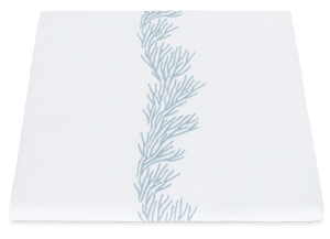 Matouk Atoll Bedding Collection, Wedgwood incorporates a white table runner made from Ceylon cotton percale, adorned with a blue coral-like embroidered pattern running vertically down the center.