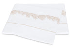 Two folded white pillowcases from the Matouk Atoll Bedding Collection, crafted from luxurious CEYLON cotton percale with a 520 thread count and adorned with a delicate beige botanical branch embroidery along the edge.