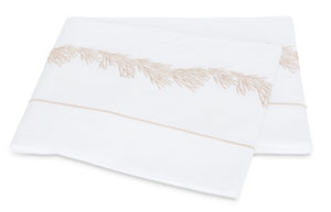 Two folded white pillowcases from the Matouk Atoll Bedding Collection, crafted from luxurious CEYLON cotton percale with a 520 thread count and adorned with a delicate beige botanical branch embroidery along the edge.
