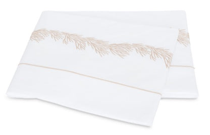 Two folded white pillowcases from the Matouk Atoll Bedding Collection, crafted from luxurious CEYLON cotton percale with a 520 thread count and adorned with a delicate beige botanical branch embroidery along the edge.