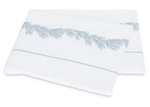 Two folded white towels from the Matouk Atoll Bedding Collection, expertly crafted from CEYLON cotton percale with a luxurious 520 thread count, showcase a delicate blue branch-like embroidered pattern and a fine blue border near the edge, all elegantly arranged on a plain background.