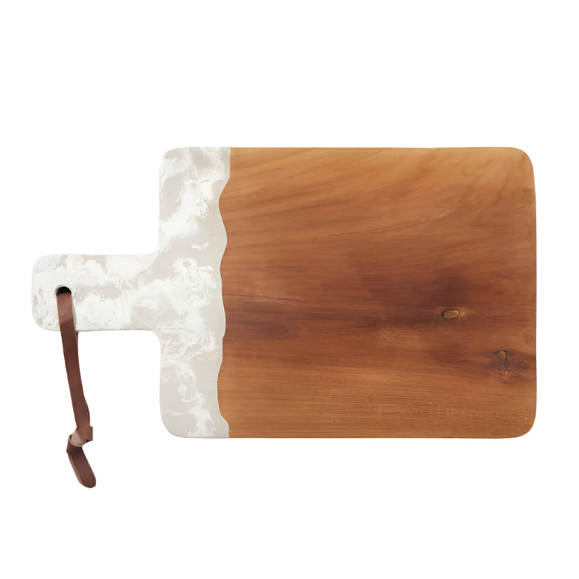The Austin Swirled Serveware Collection by Blue Pheasant features a rectangular handcrafted wooden cutting board with a handle, a white marbled resin accent on one side, and a brown leather loop on the handle.