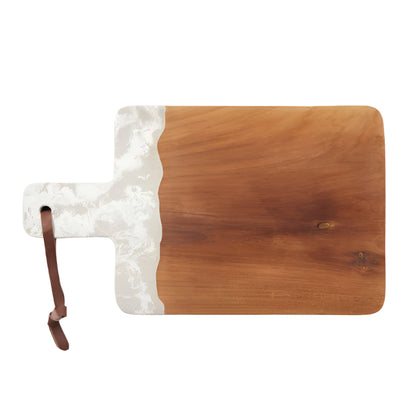 The Austin Swirled Serveware Collection by Blue Pheasant features a rectangular handcrafted wooden cutting board with a handle, a white marbled resin accent on one side, and a brown leather loop on the handle.