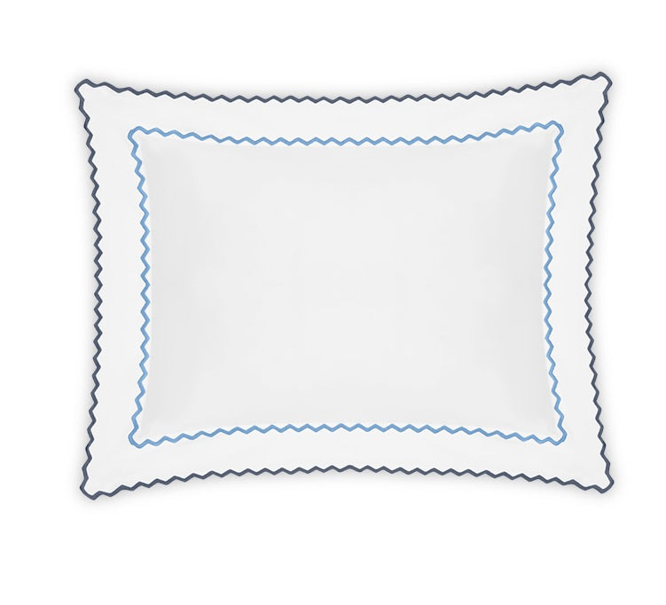 The Axel Bedding Collection by Matouk features a white rectangular pillow adorned with blue and navy scalloped trim along the edges, meticulously crafted from soft long-staple cotton and finished with subtle zigzag embroidery. Displayed on a white background, this pillow serves as the perfect accent for any modern bed.