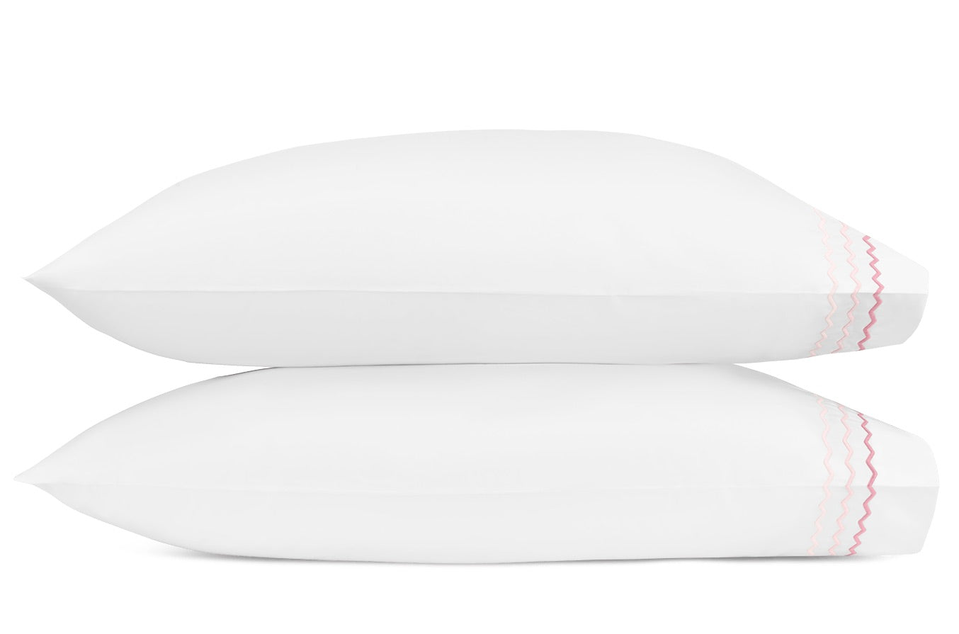 Two white pillows from the Axel Bedding Collection by Matouk are stacked on top of each other, each crafted from long-staple cotton and accented with a pink wavy stitched line near one edge, set against a plain white background.