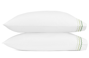 Two white pillows from the Matouk Axel Bedding Collection, Spring Green, crafted from long-staple cotton with green zigzag embroidery on the edge—ideal for a modern bed.
