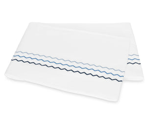 Folded white bedsheet from the Axel Bedding Collection by Matouk, featuring two zigzag embroidered lines—one light blue and one dark blue—near the edge. Crafted from long-staple cotton, this sheet adds a refined touch to any modern bed with its elegant embroidery detailing.