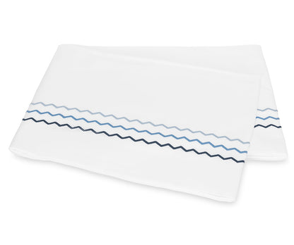 Folded white bedsheet from the Axel Bedding Collection by Matouk, featuring two zigzag embroidered lines—one light blue and one dark blue—near the edge. Crafted from long-staple cotton, this sheet adds a refined touch to any modern bed with its elegant embroidery detailing.