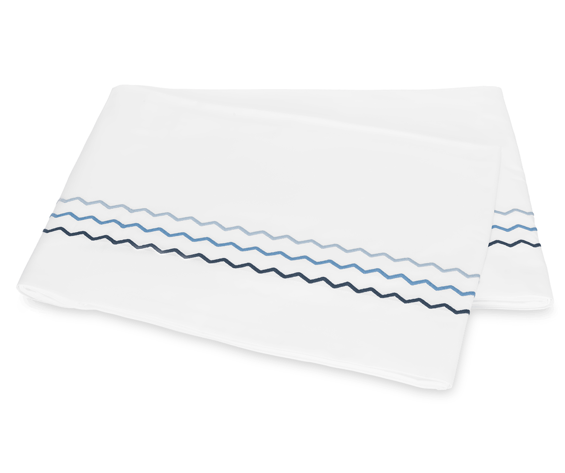 Two folded white pillowcases from the Matouk Axel Bedding Collection, Azure, feature blue and navy zigzag embroidery near the edge and are displayed on a plain background for a modern touch.