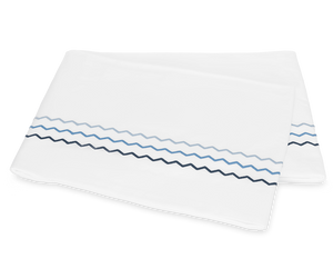 Two folded white pillowcases from the Matouk Axel Bedding Collection, Azure, feature blue and navy zigzag embroidery near the edge and are displayed on a plain background for a modern touch.