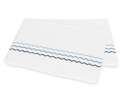 Two folded white pillowcases from the Matouk Axel Bedding Collection, Azure, feature blue and navy zigzag embroidery near the edge and are displayed on a plain background for a modern touch.