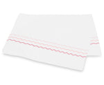 Two white rectangular cloths from the Axel Bedding Collection by Matouk, crafted from luxurious long-staple cotton, feature pink and red zigzag embroidery along one edge and are stacked slightly askew on a white background.