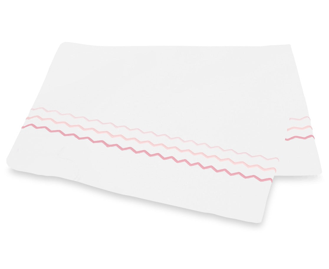 Two white rectangular cloths from the Axel Bedding Collection by Matouk, crafted from luxurious long-staple cotton, feature pink and red zigzag embroidery along one edge and are stacked slightly askew on a white background.
