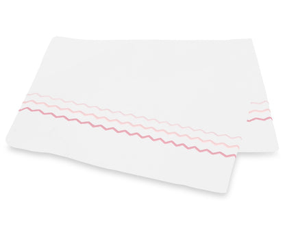Two white rectangular cloths from the Axel Bedding Collection by Matouk, crafted from luxurious long-staple cotton, feature pink and red zigzag embroidery along one edge and are stacked slightly askew on a white background.
