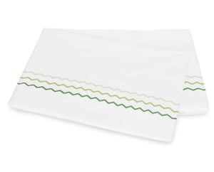 Two folded white pillowcases from the Axel Bedding Collection by Matouk, featuring green zigzag embroidery along one edge, crafted from luxurious long-staple cotton—a crisp, modern bed essential.