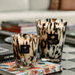 Two decorative Baobab Collection Pearls Black Candles with leopard print designs placed on a coffee table with books are enhanced by the Ginger Grapefruit Rose scent.