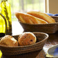 Calaisio's Oval Bread Basket Collection holds an array of fresh bread rolls and baguettes on a wooden table, accompanied by bottles of olive oil and a folded blue napkin.