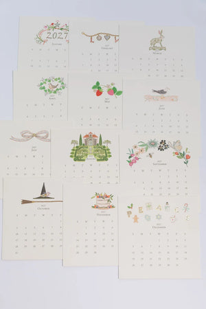 Twelve monthly Karen Adams 2027 Classic Desk Calendar cards, each featuring unique seasonal illustrations above the dates.