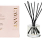 A pink box labeled "Blushed Bergamot Scent Collection" by L’Avant Collective sits beside a reed diffuser filled with liquid and black reeds, offering an uplifting citrus-inspired fragrance.